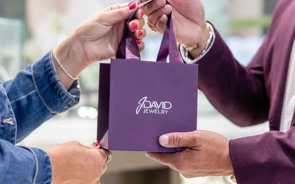 A purple J. David bag passing from one pair of hands to another