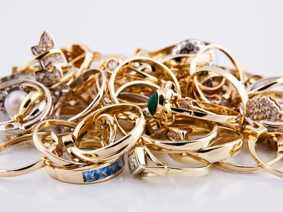 A small pile of gold rings, some set with gems, on a white surface