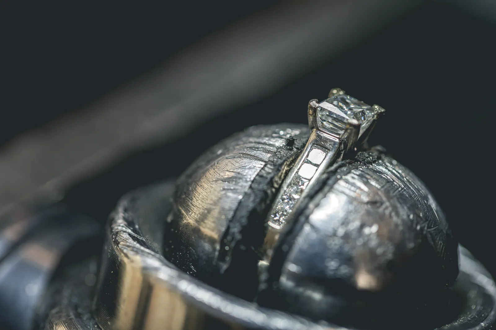 A ring held in the bench clamp while the seam is finished, its chipped diamonds visible along the band