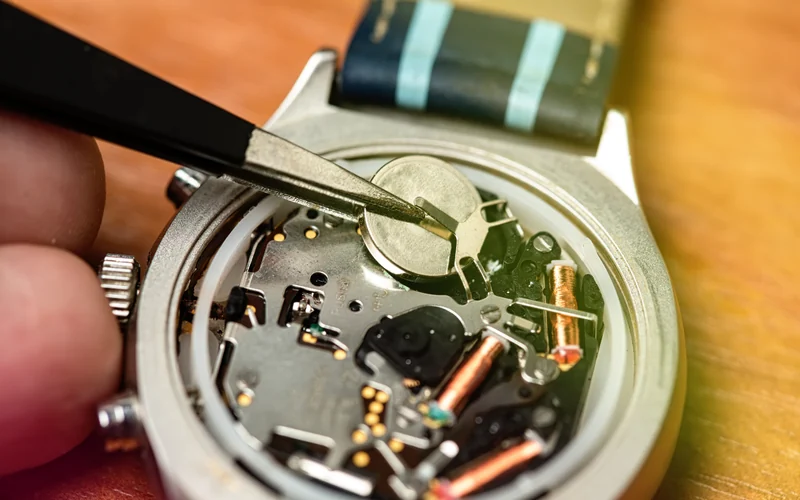 A watch battery lifted out with tweezers