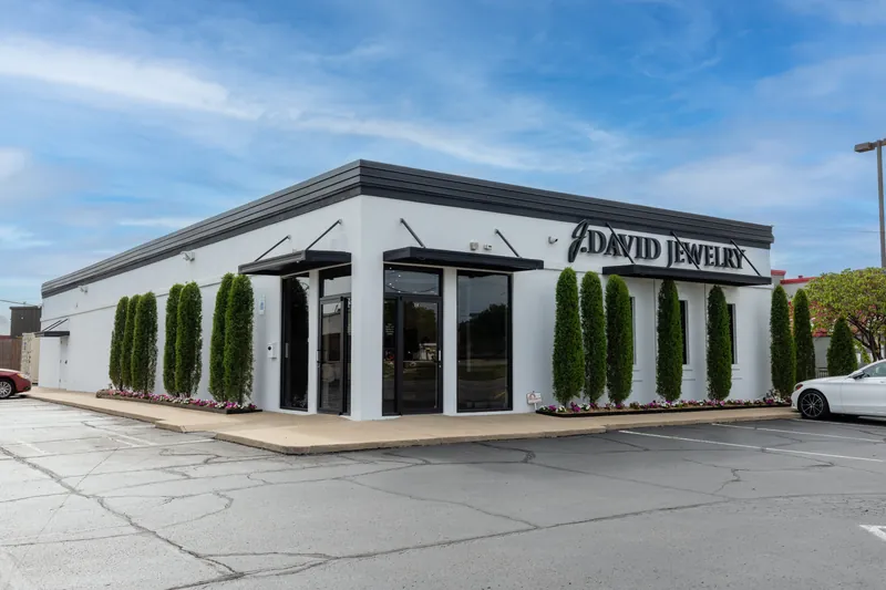 The Broken Arrow showroom: a white building with black J. David Jewelry letters, lined with tall evergreens
