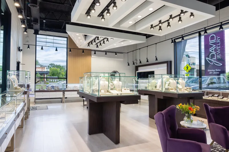 Glass cases by tall windows full of daylight, with plum velvet chairs and flowers on a small table