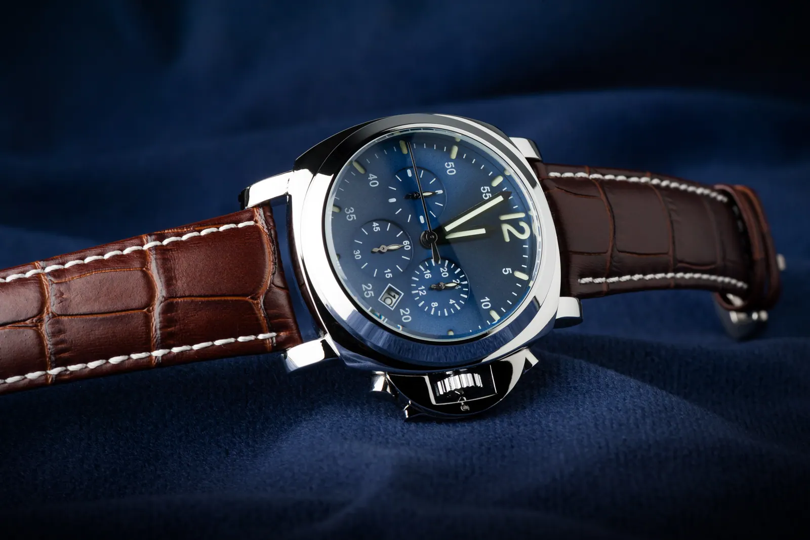 A steel chronograph with a blue dial and a brown leather strap, resting on navy velvet
