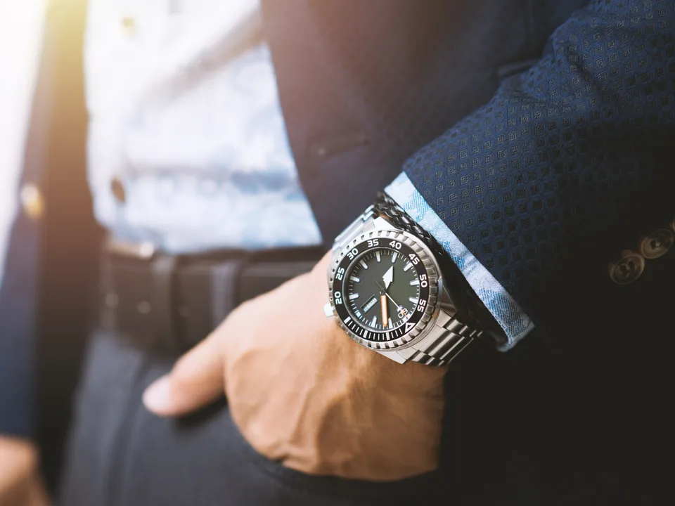 A steel diver on the wrist under a navy jacket cuff, hand in pocket