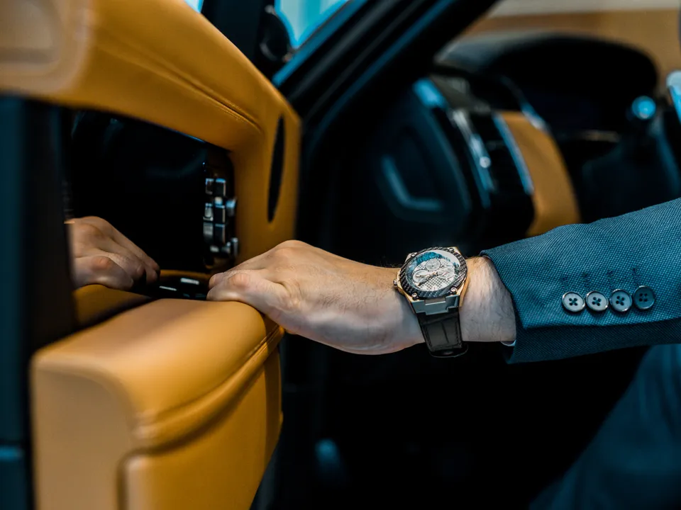 A chronograph on a wrist, the hand resting on a car door