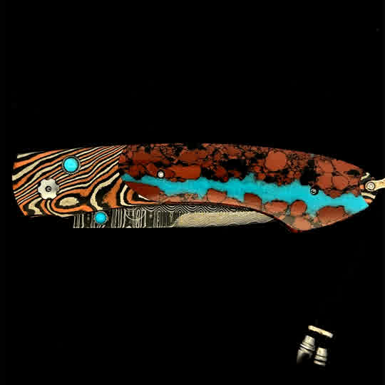 William Henry Knife The Spearpoint 'Chuska' features a beautiful frame in 'Twist' Mokume by Mike Sakmar, inlaid with vein turquoise. The blade is William Henry's signature 'Wave' damascus steel with VG-10 core. The one-hand button lock and the thumb stud